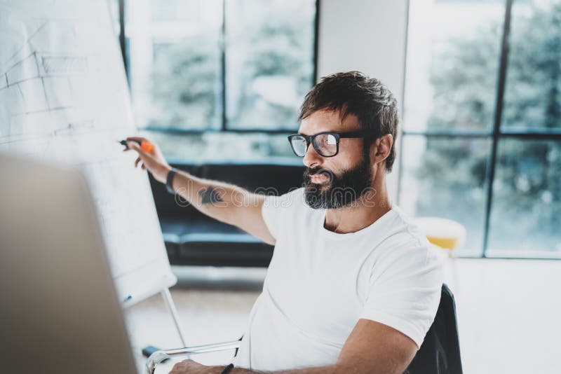 Young bearded man wearing eye glasses and working at sunny office.Blurred background. Horizontal. Cropped. stock images Young bearded man wearing eye glasses and working at sunny office.Blurred background. Horizontal. Cropped. stock images