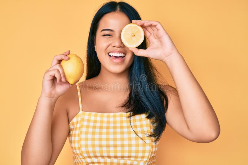 Young beautiful asian girl holding lemon smiling and laughing hard out loud because funny crazy joke