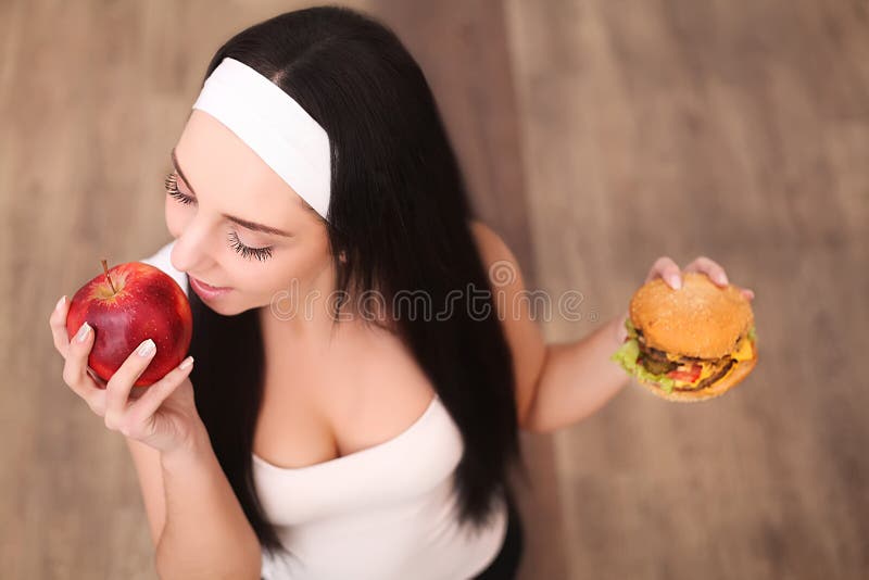 Young beautiful asian girl making choice between hamburger and a red apple, healthy eating and lifestyle concept. stock photo Young beautiful asian girl making choice between hamburger and a red apple, healthy eating and lifestyle concept. stock photo