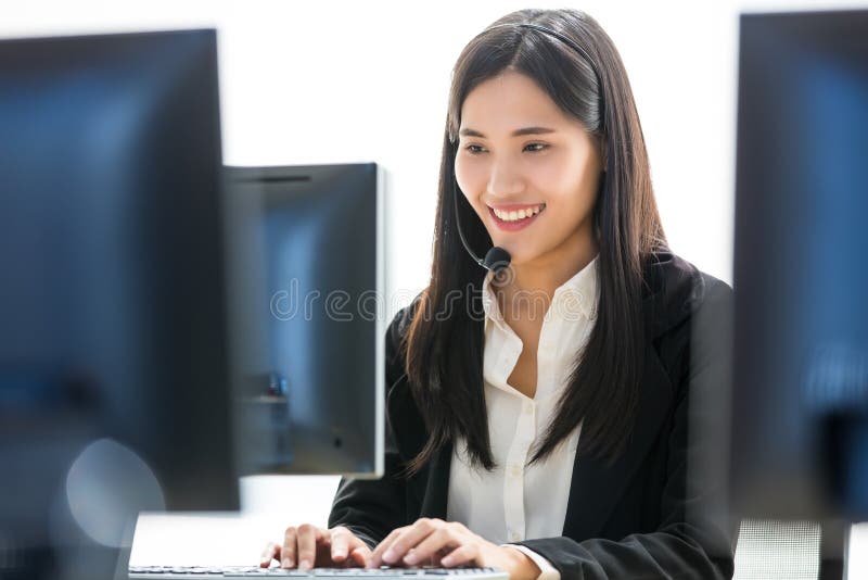 Young and beautiful Asian woman call center officer wearing microphone headset and happy working with a friendly face and positive