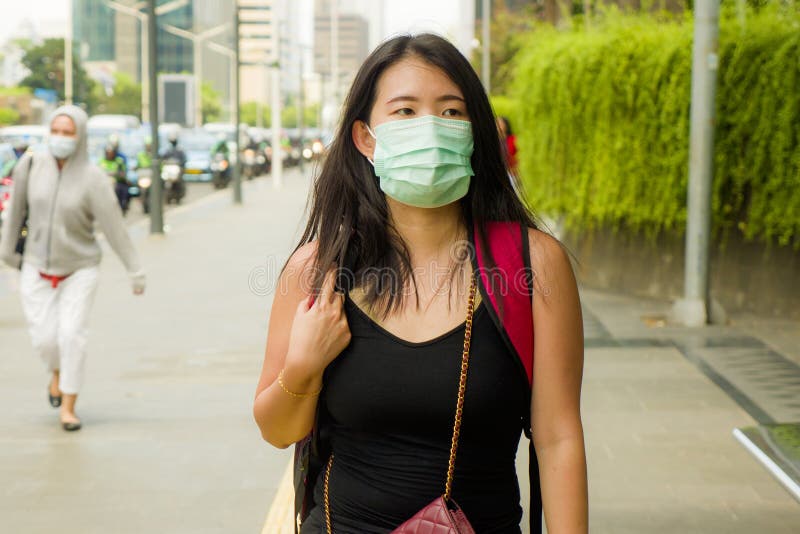 Young beautiful and attractive Asian Chinese student woman walking on city street wearing protective facial mask against China stock photo Young beautiful and attractive Asian Chinese student woman walking on city street wearing protective facial mask against China stock photo