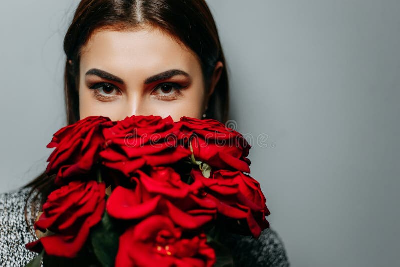 Young beautiful attractive woman hiding behind red roses. Girl w