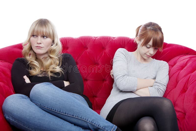Young beautiful blond and red haired girls on red sofa have a co stock images