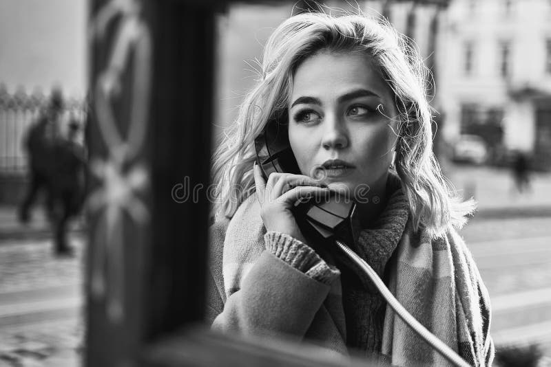 Young beautiful blond woman making an important call in a vintage public phone booth on a sunny evening