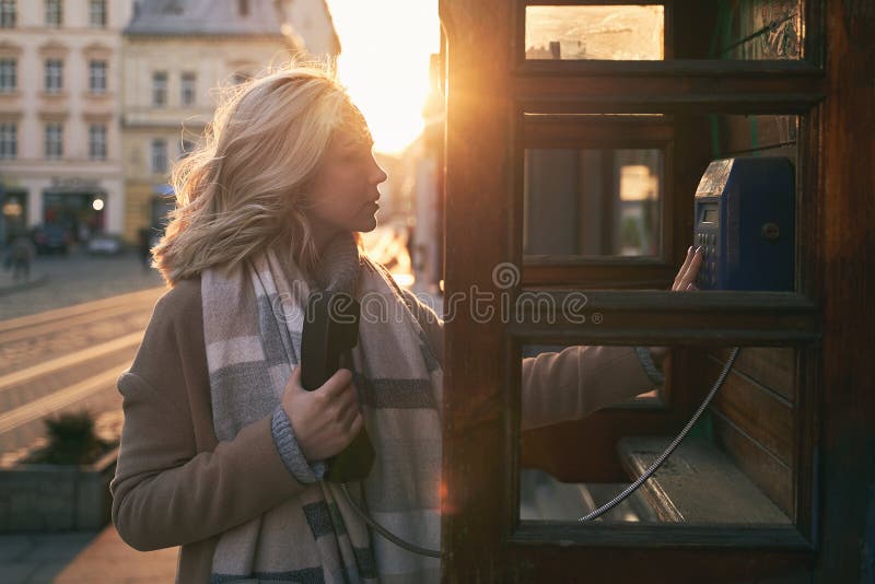 Young beautiful blond woman ready to make an important call in a vintage public phone booth on a sunny evening