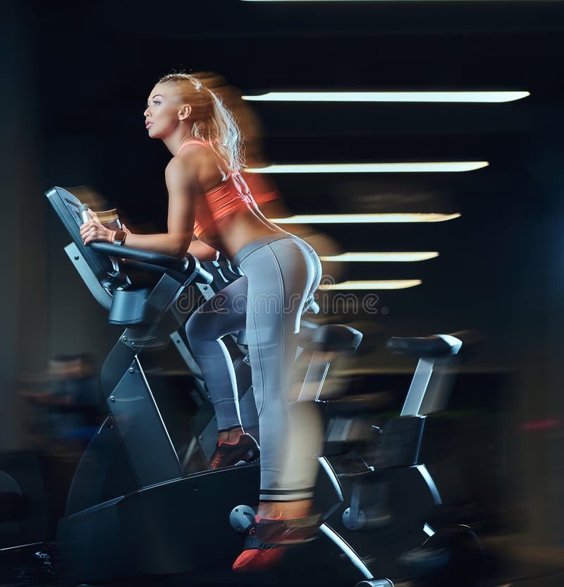 Young beautiful blonde woman in sportswear training on an exercise bike in modern fitness center.