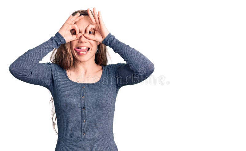 Young beautiful blonde woman wearing casual dress doing ok gesture like binoculars sticking tongue out, eyes looking through