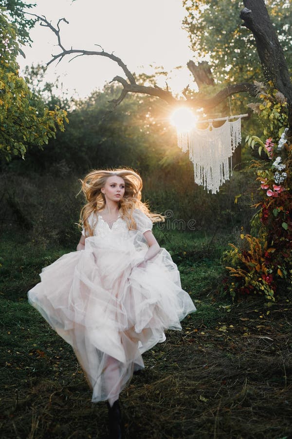 A young beautiful blonde woman in a white dress spins and dances in a clearing in the forest. Attractive fashion model