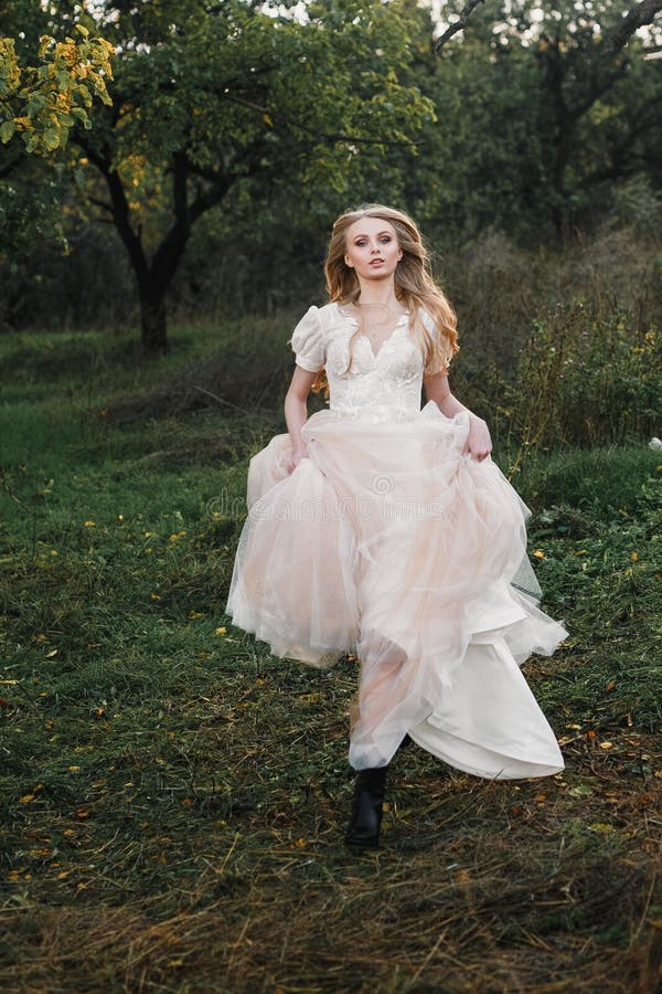 A young beautiful blonde woman in a white dress spins and dances in a clearing in the forest. Attractive fashion model