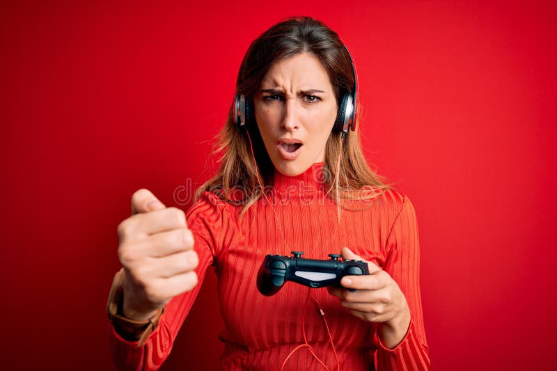 Young beautiful brunette gamer woman playing video game using joystic and headphones annoyed and frustrated shouting with anger