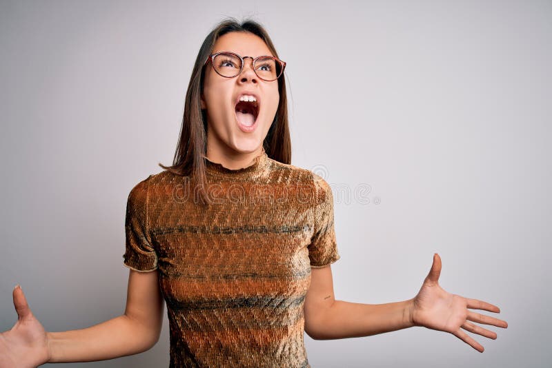 Young beautiful brunette girl wearing casual t-shirt and glasses over isolated white background crazy and mad shouting and yelling