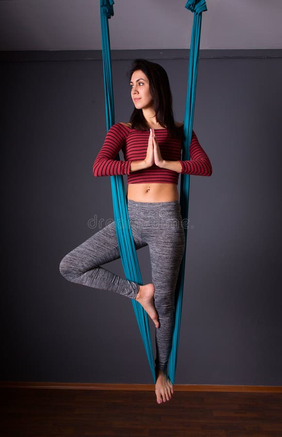 young beautiful brunette woman doing fly yoga. Sitting in hammock with namaste gesture. Wellness concept.