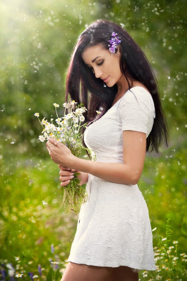 Young beautiful brunette woman holding a wild flowers bouquet in a sunny day. Portrait of attractive long hair female in white