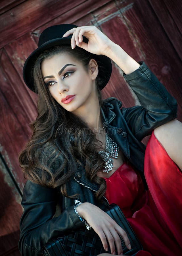 Young beautiful brunette woman with red short dress and black hat posing sensual in vintage scenery. Romantic mysterious lady