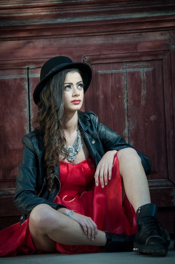 Young beautiful brunette woman with red short dress and black hat posing sensual in vintage scenery. Romantic mysterious lady