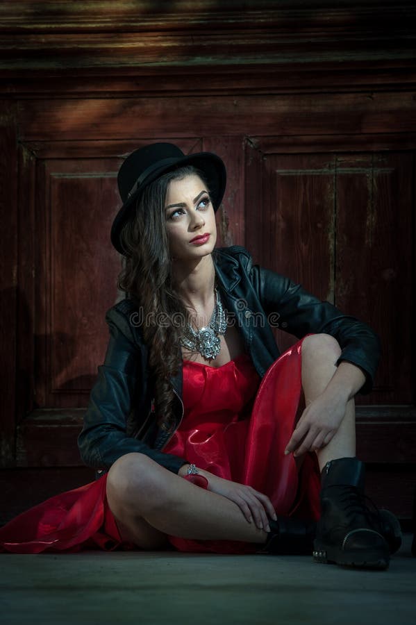 Young beautiful brunette woman with red short dress and black hat posing sensual in vintage scenery. Romantic mysterious lady