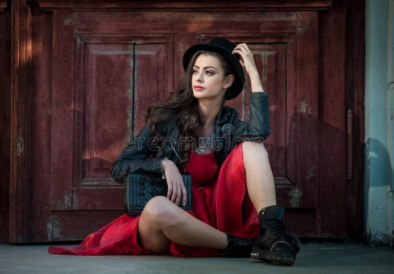 Young beautiful brunette woman with red short dress and black hat posing sensual in vintage scenery. Romantic mysterious lady