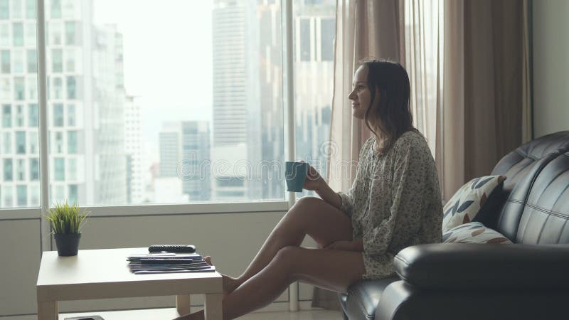 Young beautiful brunette woman sits on the sofa puts her feet on table and relaxes. The girl watches TV by the window royalty free stock photos Young beautiful brunette woman sits on the sofa puts her feet on table and relaxes. The girl watches TV by the window royalty free stock photos