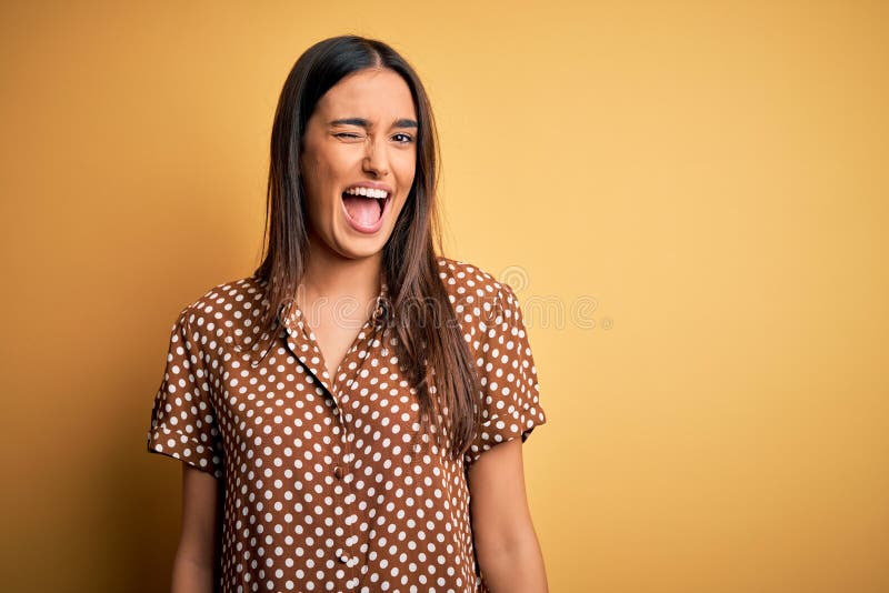 Young beautiful brunette woman wearing casual shirt over isolated yellow background winking looking at the camera with sexy