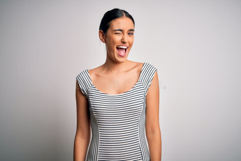 Young beautiful brunette woman wearing casual striped dress over isolated white background winking looking at the camera with sexy