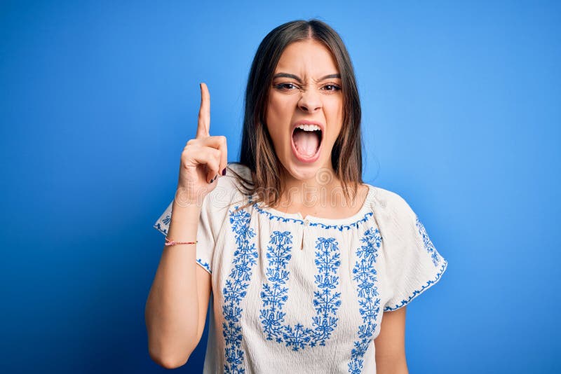 Young beautiful brunette woman wearing casual t-shirt standing over blue background pointing finger up with successful idea