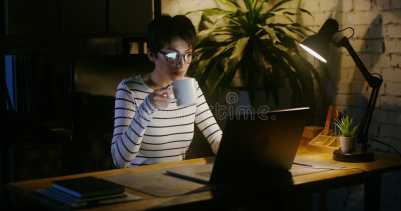 Young businesswoman drinks coffee while working at a laptop in office