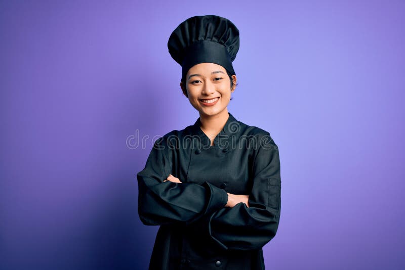 Young beautiful chinese chef woman wearing cooker uniform and hat over purple background happy face smiling with crossed arms