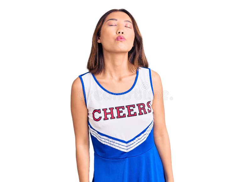 Young beautiful chinese girl wearing cheerleader uniform looking at the camera blowing a kiss on air being lovely and sexy. love expression