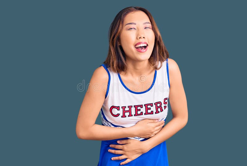 Young beautiful chinese girl wearing cheerleader uniform smiling and laughing hard out loud because funny crazy joke with hands on