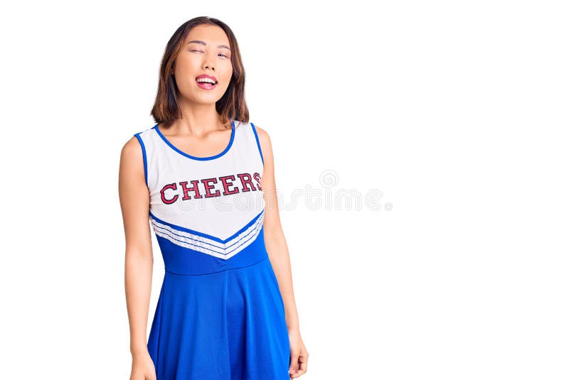 Young beautiful chinese girl wearing cheerleader uniform winking looking at the camera with sexy expression, cheerful and happy face