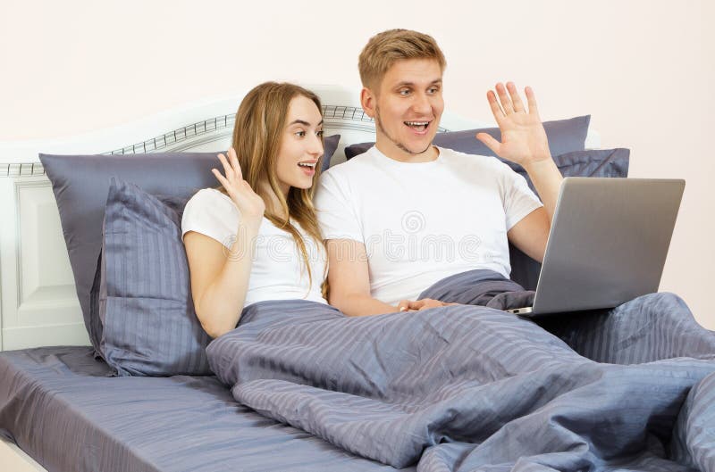 Young beautiful couple lying on bed in bedroom and talking on the laptop using video chat stock image Young beautiful couple lying on bed in bedroom and talking on the laptop using video chat stock image
