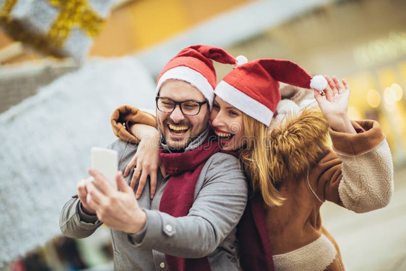 Beautiful couple with Santa hats make selfie photo in the city stock image Beautiful couple with Santa hats make selfie photo in the city stock image