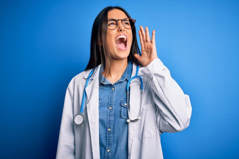 Young beautiful doctor woman wearing stethoscope and glasses over blue background shouting and screaming loud to side with hand on