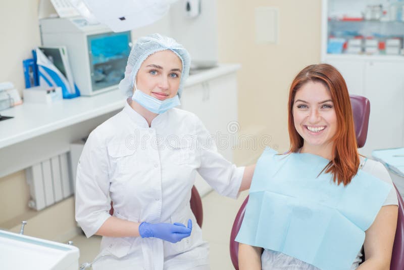 Young beautiful female dentist helps patient with toothache. Red-haired woman sits in a chair at the doctor on examination. Dental