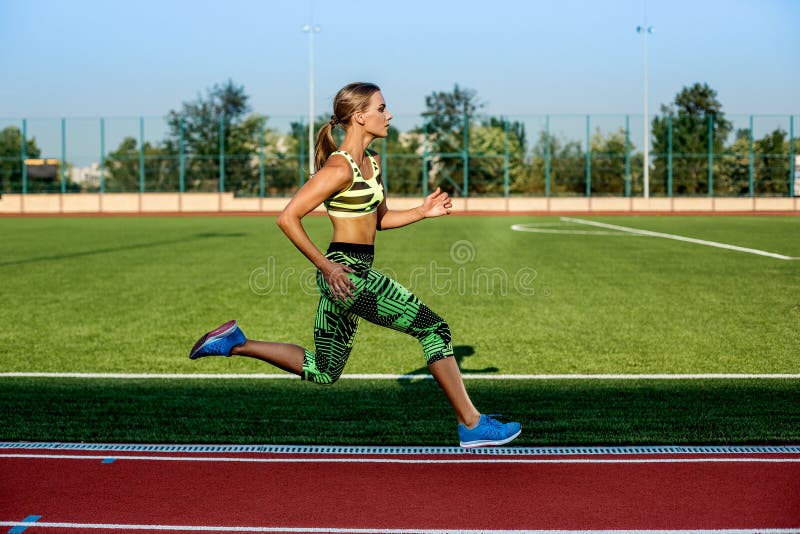Young, beautiful girl athlete in sportswear runs along the treadmill. Sport background. Outdoor stadium. Young, beautiful girl athlete in sportswear runs along the treadmill. Sport background. Outdoor stadium