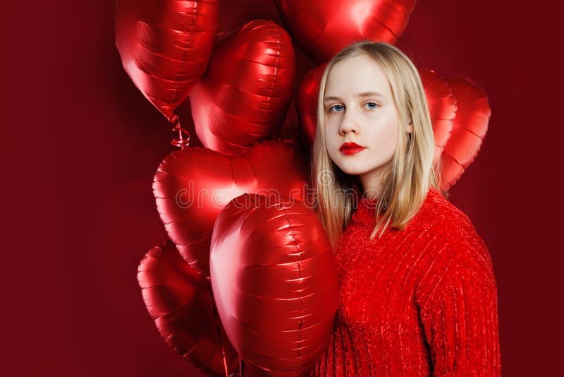 Young beautiful girl holds balloons red heart on red background