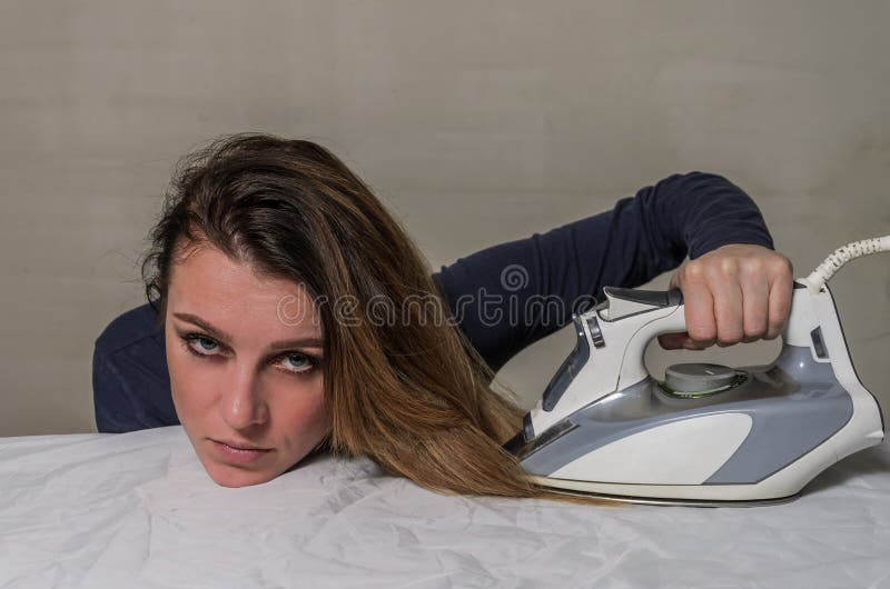 Young beautiful girl ironing her hair on an ironing board