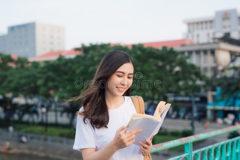 Young beautiful girl reading book on a bridge with city view