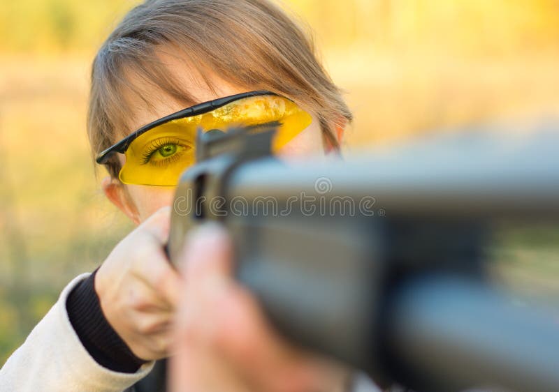 A young girl with a gun for trap shooting and shooting glasses aiming at a target. A young girl with a gun for trap shooting and shooting glasses aiming at a target