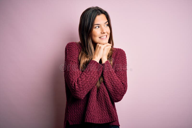 Young beautiful girl wearing casual sweater over isolated pink background laughing nervous and excited with hands on chin looking