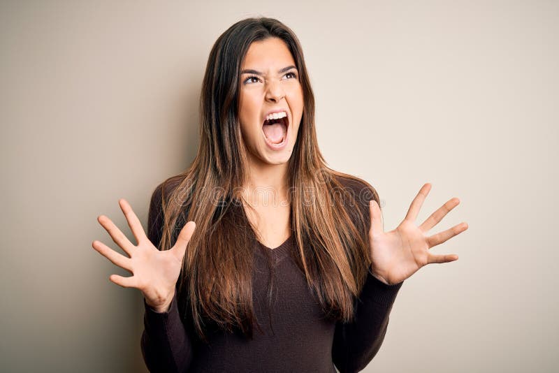 Young beautiful girl wearing casual sweater standing over isolated white background crazy and mad shouting and yelling with