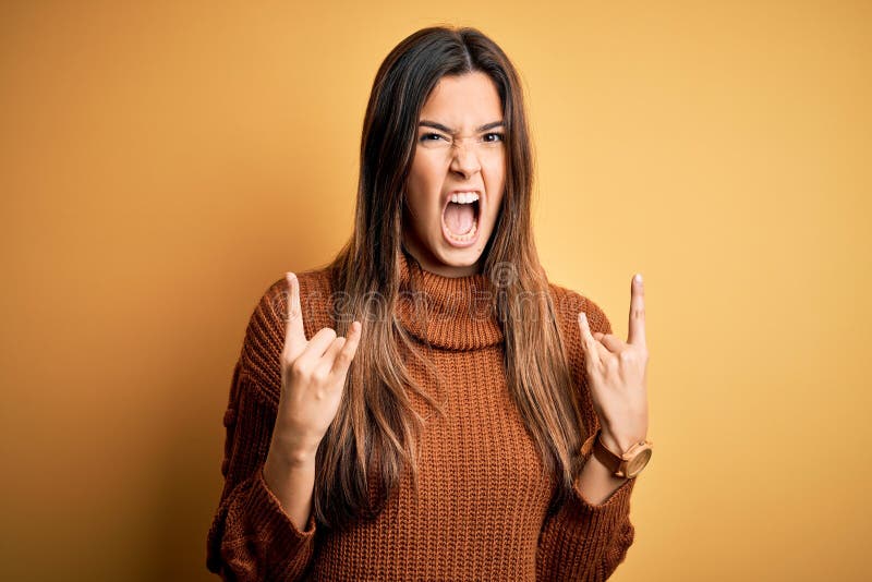 Young beautiful girl wearing casual sweater standing over isolated yellow background shouting with crazy expression doing rock