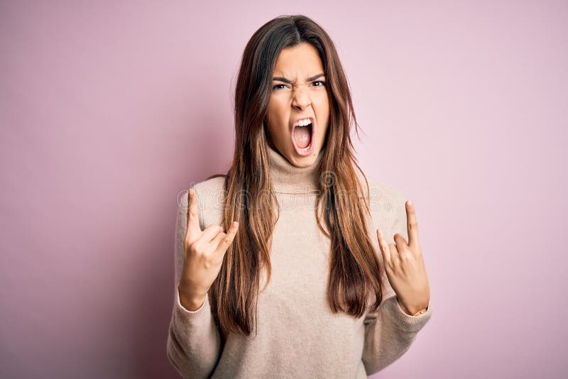 Young beautiful girl wearing casual turtleneck sweater standing over isolated pink background shouting with crazy expression doing