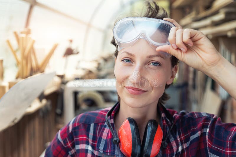 Young beautiful handy professional happy female strong carpenter portrait wearing protective goggles working in
