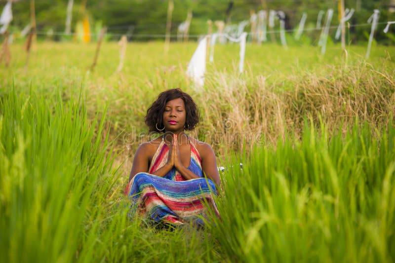 Young beautiful and happy black African American woman sitting at rive field outdoors practicing yoga relaxation and meditation