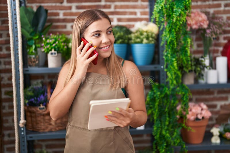 Young beautiful hispanic woman florist talking on smartphone reading notebook at florist stock photos