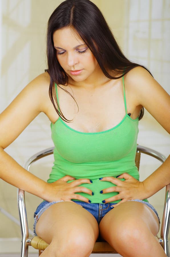 Young beautiful hispanic woman with green blouse touching her belly with both hands, with half opened arms suffering royalty free stock photos Young beautiful hispanic woman with green blouse touching her belly with both hands, with half opened arms suffering royalty free stock photos
