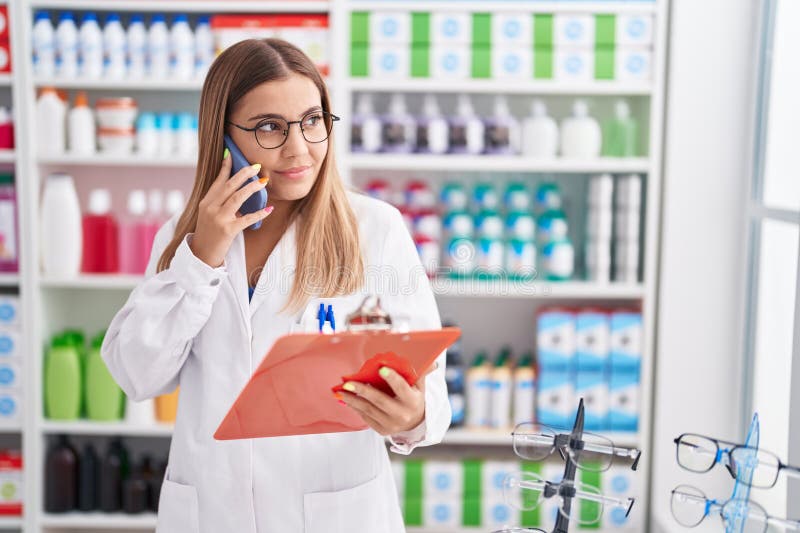 Young beautiful hispanic woman pharmacist talking on smartphone reading document at pharmacy stock photography