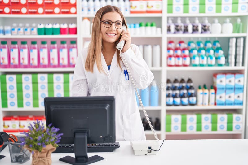 Young beautiful hispanic woman pharmacist talking on telephone using computer at pharmacy stock images