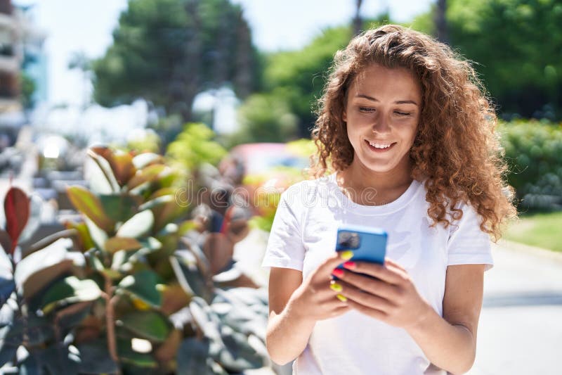 Young beautiful hispanic woman smiling confident using smartphone at park stock photography